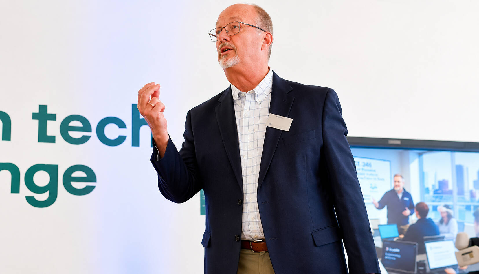 Paul Hillman stands with right arm raised during a presentation at the front of a room